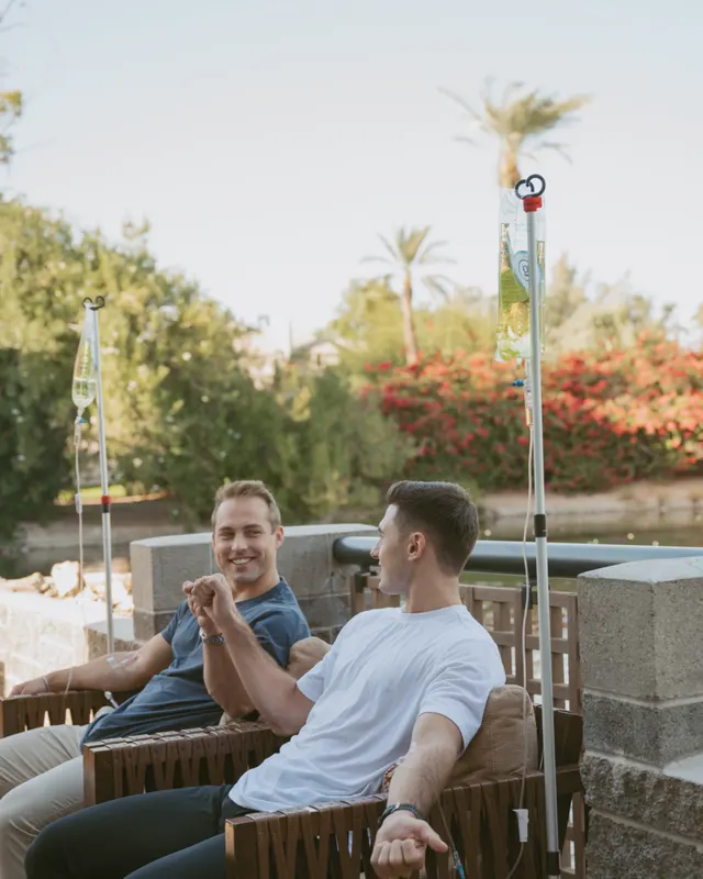 Two friends relaxing with their IVs on a resort patio under the palms
